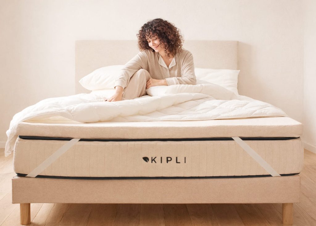 Donna seduta sul letto con il topper Kipli in lattice fissato con gli elastici