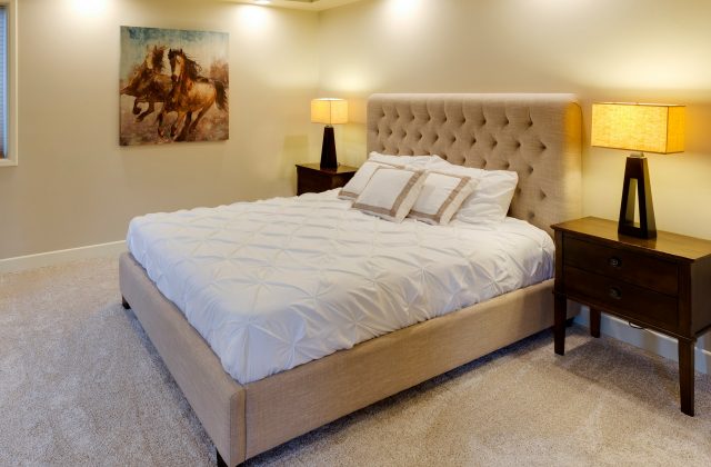 Letto matrimoniale con testiera imbottita, materasso coperto da un piumino bianco e due comodini con lampade